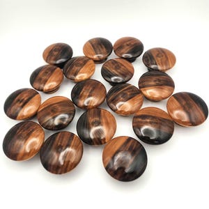 Peut inclure: Ensemble de boutons de meubles ronds en bois. Chaque bouton présente un motif tourbillonnant de grain de bois brun foncé et brun clair. Les boutons sont lisses et polis, de forme légèrement bombée.