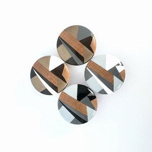 Op de afbeelding: Vier ronde houten knoppen met geometrische patronen in zwart, wit, grijs en bruin.