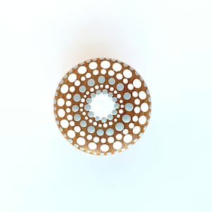 May include: A round, wooden decorative object with a mandala-style dot pattern. The design features white and light blue dots on a brown background, with a white center. The object is likely a decorative element for home decor.