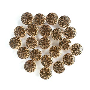Może przedstawiać: Kolekcja dwudziestu czterech drewnianych gałek do szafek z kwiatowym wzorem. Każda gałka jest okrągła, z jasnobrązową podstawą i czarnym, skomplikowanym wzorem kwiatowym. Gałki ułożone są na białym tle.
