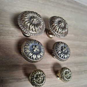 Könnte beinhalten: Satz von sechs antiken Messing-Schrankknöpfen mit floralem Design. Die Knöpfe sind rund und haben eine erhabene Mitte mit einem kleinen Blumendesign. Die Knöpfe sind in verschiedenen Größen.