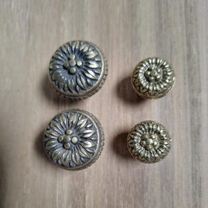 May include: Four brass knobs with a floral design. The knobs are different sizes and have a slightly aged finish.