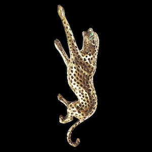 May include: A gold-toned metal brooch in the shape of a leaping leopard. The leopard has a spotted pattern and green eyes.