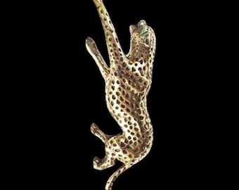 May include: A gold-toned metal brooch in the shape of a leaping leopard. The leopard has a spotted pattern and green eyes.
