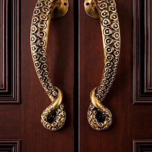 May include: A pair of brass-colored door handles, each shaped like an octopus tentacle. The handles are mounted on a dark brown wooden door. The tentacles have a textured surface with circular details, and the handles curve gracefully.
