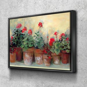 Op de afbeelding: Een ingelijste canvas print met een rij potgeraniums met felrode bloemen en groene bladeren. De terracotta potten staan tegen een zachte gele en groene achtergrond, wat een warme, uitnodigende scène creëert.
