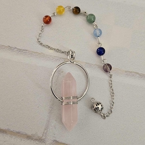 May include: A pink rose quartz crystal pendulum with a silver chain and a circle charm. The chain has seven beads in rainbow colors.