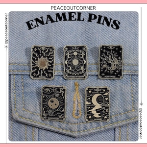 May include: Set of eight enamel pins featuring tarot card imagery. The pins are black and white with silver accents. The cards depicted are The Sun, The Wheel of Fortune, The Lovers, The Magician, and The Moon.