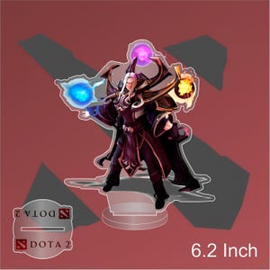 Op de afbeelding: Een 15,7 cm hoge acrylstandaard met een Dota 2-personage met wit haar, een paarse robe en een staf. Het personage wordt omringd door drie gloeiende bollen, een blauwe, een paarse en een oranje.