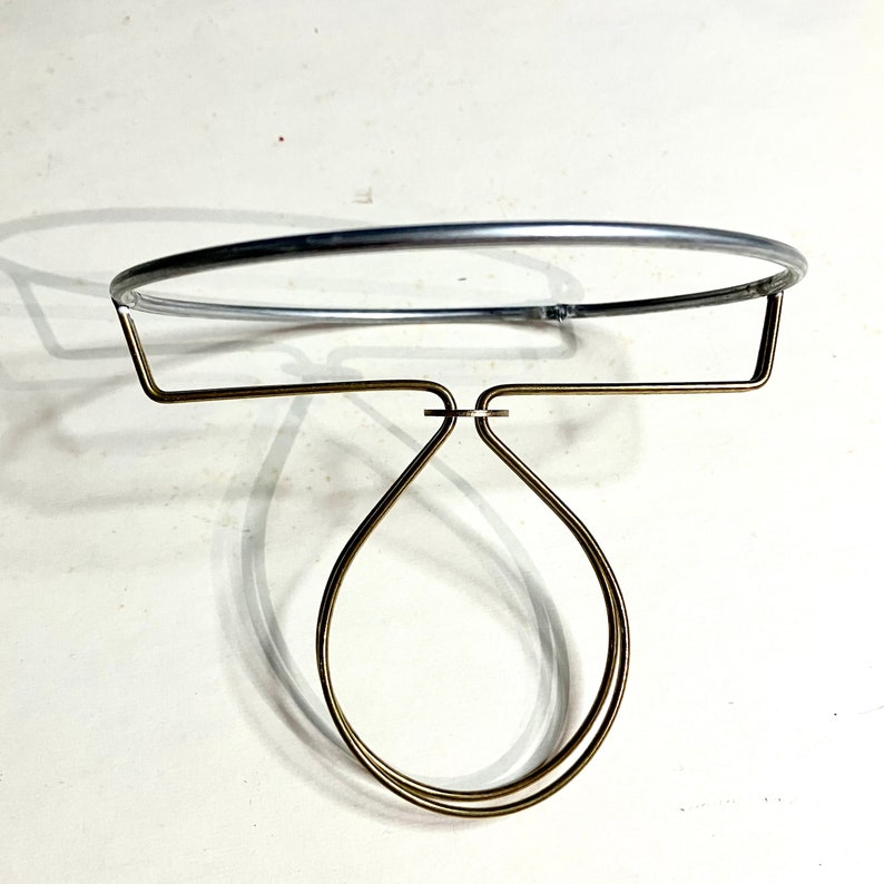 May include: A silver lampshade clip on ring with a brass adjustable holder. The holder has a double loop design that fits over a lightbulb.