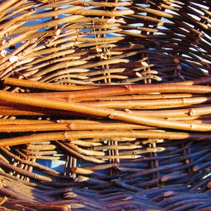 May include: A woven wicker basket with a natural brown finish. The basket is filled with long, thin, brown sticks.
