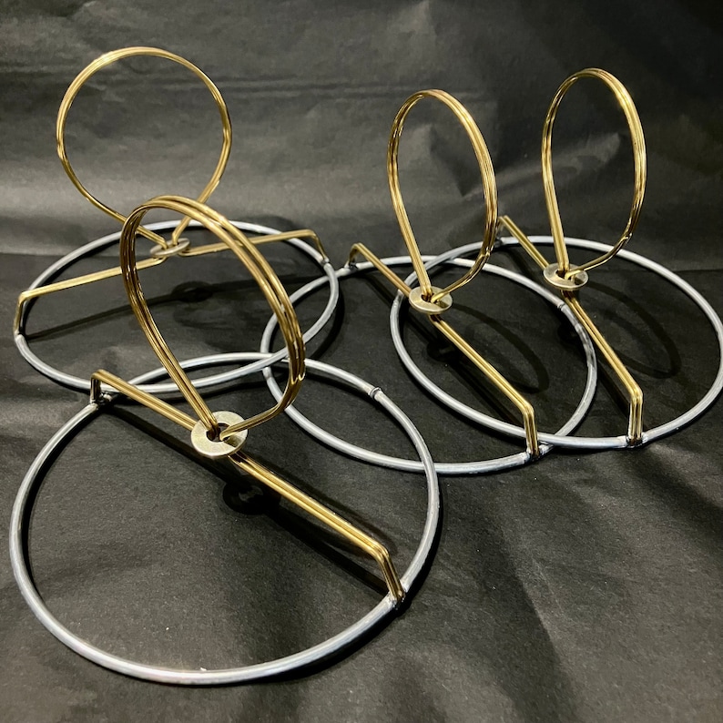 May include: Four lampshade rings, two gold and two silver, are stacked on top of each other. The rings are made of metal and have a circular shape.