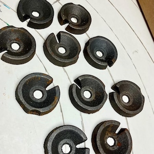 May include: A collection of ten dark, circular metal objects with a central hole and a notch cut out of the side. The objects appear to be made of cast iron and have a slightly rusted appearance, suggesting age or exposure to the elements.