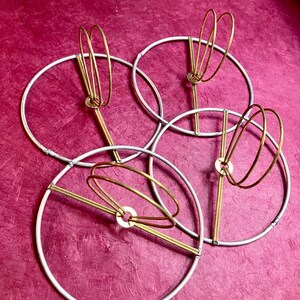 May include: Four flush clip top lampshade hardware. silver galvanized steel 11 gauge hoops with brass wire circles in the center.
