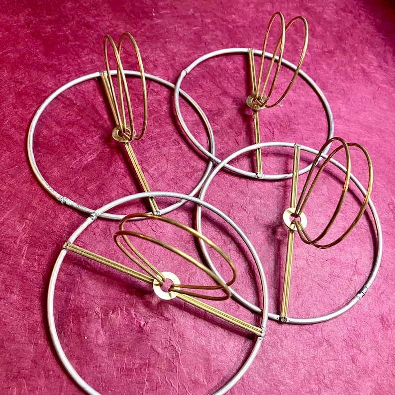 May include: Four flush clip top lampshade hardware. silver galvanized steel 11 gauge hoops with brass wire circles in the center.