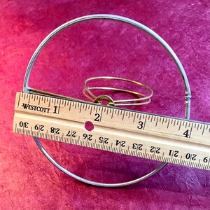 May include: A silver metal clip top lampshade ring with a brass ring inside. The ring is 3 inches in diameter.