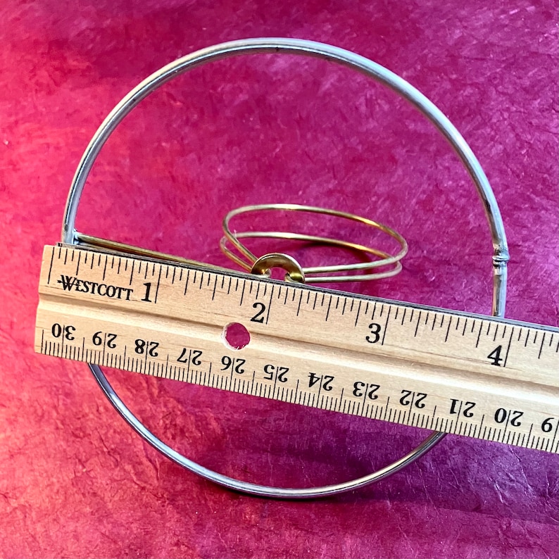 May include: A silver metal clip top lampshade ring with a brass ring inside. The ring is 3 inches in diameter.