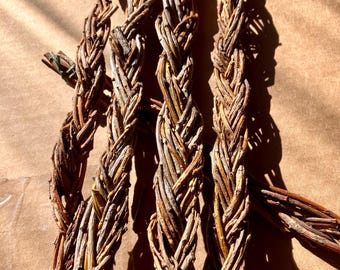 Puede incluir: Tres largas y delgadas hebras de ramas de sauce marrón trenzadas juntas en una cuerda gruesa y texturizada. La madera natural muestra tonos variados de marrón claro y oscuro, con una superficie orgánica rugosa y nudos visibles.