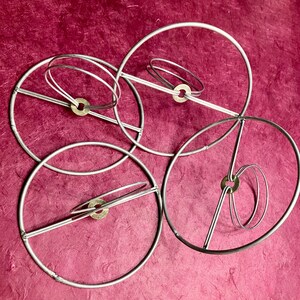 May include: A set of four silver metal hoops, each with a different diameter, are intertwined and connected by small brass rings. The hoops are arranged in a circular pattern, creating a decorative and abstract design.
