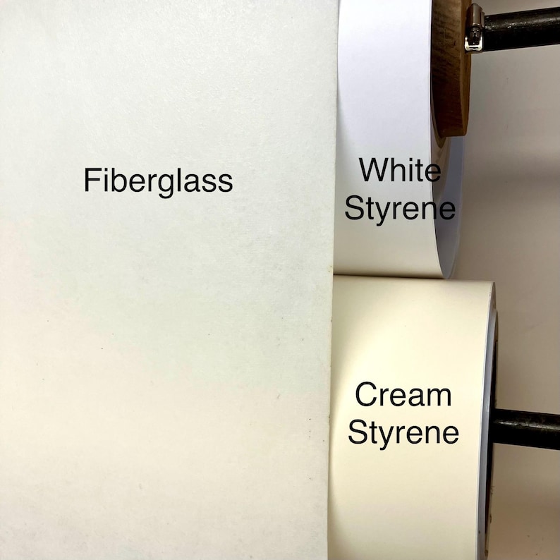 May include: Three rolls of material mounted on a horizontal bar. The left roll is labeled Fiberglass and is off-white. The top right roll is labeled White Styrene and is bright white. The bottom right roll is labeled Cream Styrene and is cream.