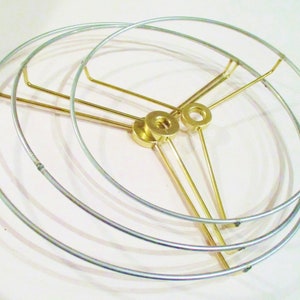 May include: A set of three gold-toned metal lampshade rings. The rings are stacked on top of each other and are connected by three gold-toned metal rods.