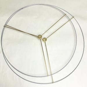 May include: A metal lampshade frame with two concentric silver rings and three gold-colored support rods. The rods converge at a central point, connected by small gold-colored rings. The frame is designed for a lampshade.