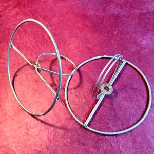 May include: Two silver metal lampshade clip tops are intertwined, creating a circular design. The hoops have a small brass piece in the center that slips over a lightbulb.