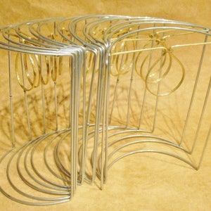 May include: A silver metal jewelry stand with multiple curved tiers. The stand is designed to hold rings, bracelets, or earrings. The stand is made of thin metal wire and has a modern, minimalist design.