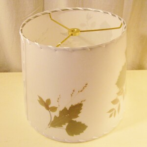 May include: A white lampshade with a gold metal frame and a design of pressed dried leaves and flowers.