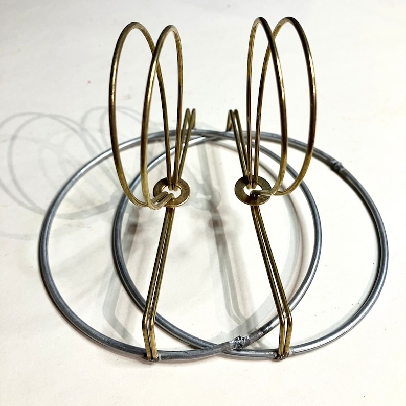 May include: A pair of clip on lampshade wires with 1/2” drop. The outer circle is galvanized steel wire and the inner wires are brass that slip over the bulb.