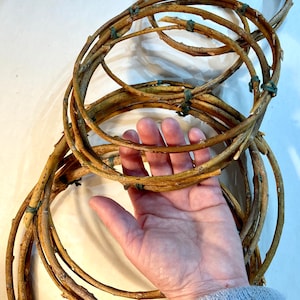 May include: A set of woven twig wreaths, tied together with green twine. The wreaths are arranged in a circular pattern, with the largest wreath in the center. The wreaths are made of natural twigs and have a rustic, earthy look.