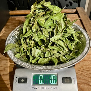 May include: A digital scale with a pile of dried green leaves in a silver bowl. The scale reads 8.00 lb.