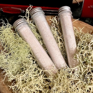 May include: Three clear glass test tubes filled with a white powder, sitting in a bed of green moss.
