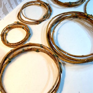 May include: Five different sized wreaths made of natural brown twigs tied together with green twine. The wreaths are arranged on a white surface.