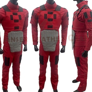 May include: Red and black jumpsuit with a chest piece and a belt. The jumpsuit has a padded chest piece with a geometric pattern and a belt with a silver buckle.