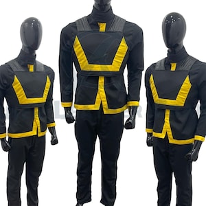 Könnte beinhalten: Drei Schaufensterpuppen tragen schwarze und gelbe Outfits. Die Outfits bestehen aus einem schwarzen Langarmhemd mit gelbem Besatz und einer schwarzen Weste mit gelbem Besatz. Die Westen haben ein geometrisches Muster.
