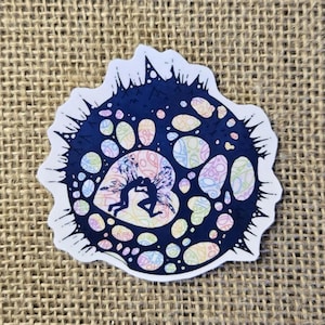 May include: A sticker with a dark blue, spiky outer design. Inside, there's a heart-shaped design with two silhouetted figures embracing. The heart is filled with pastel-colored paisley patterns. The sticker has a white border.