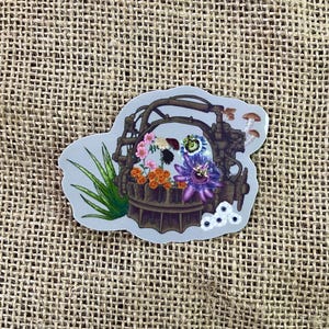 May include: A sticker featuring a detailed illustration of a diving helmet with a variety of flowers and plants growing inside. The helmet is rusty and has a dark brown color. The flowers are colorful and include purple, pink, white, yellow, and orange.