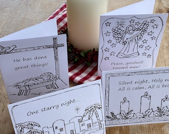 May include: Four white folded greeting cards with black line art illustrations and text. One card shows a manger scene with 'He has done great things!', another an angel with 'Peace, goodwill toward men!', a third with 'One starry night...', and the last with candles and 'Silent night, Holy night. All is calm, All is bright.'