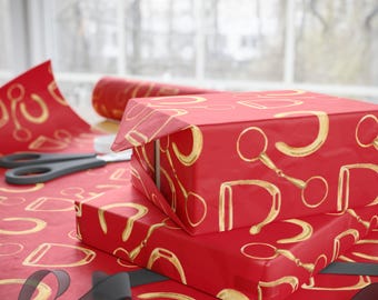May include: Two red gift boxes wrapped in red wrapping paper with a gold horseshoe pattern. The boxes are stacked on top of each other and are sitting on a table covered in the same wrapping paper.