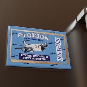 May include: A rectangular magnet with a light blue background featuring a cartoon airplane and the text "P3 ORION NAVAL AVIATION". The magnet also includes the text "OFFICIALLY MAINTAINED BY PRAYER AND DUCT TAPE" and the name "NATHAN".