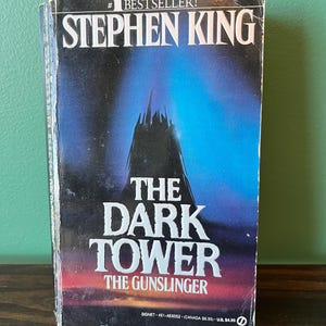 May include: A paperback book titled "The Dark Tower: The Gunslinger" by Stephen King. The cover features a dark tower silhouette against a blue and red gradient background. The book is a bestseller.