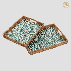 May include: Two rectangular serving trays with woven brown sides and handles. The interior of each tray features a white background with a teal floral pattern. The trays are designed to be nested together.