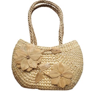 Pu&ograve; includere: Una borsa tote in paglia intrecciata con manici intrecciati e abbellimenti floreali. La borsa presenta due grandi applicazioni floreali a strati e un piccolo accento a forma di foglia. Il colore beige naturale e la trama strutturata le conferiscono un'estetica rustica ed estiva.