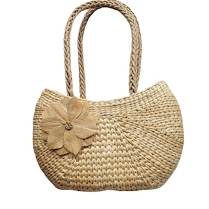 Pu&ograve; includere: Borsa tote in paglia intrecciata color beige chiaro, con manico intrecciato e un grande fiore decorativo. La borsa ha una forma arrotondata. Il fiore &egrave; fatto dello stesso materiale di paglia.