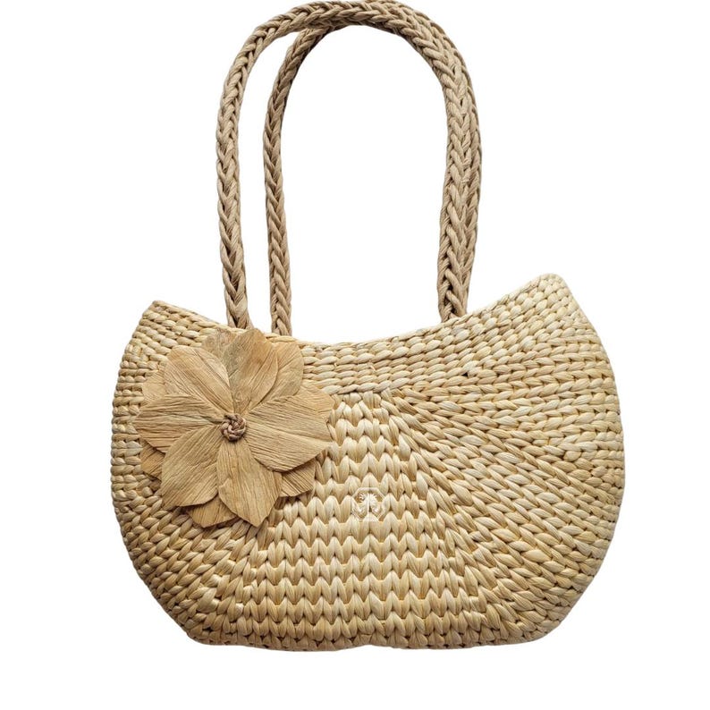 Pu&ograve; includere: Borsa tote in paglia intrecciata color beige chiaro, con manico intrecciato e un grande fiore decorativo. La borsa ha una forma arrotondata. Il fiore &egrave; fatto dello stesso materiale di paglia.