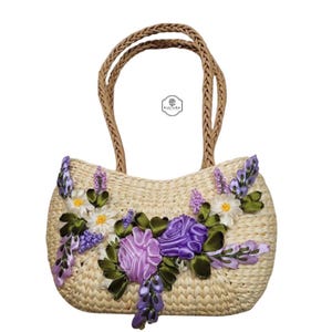 Pu&ograve; includere: Borsa a mano in paglia intrecciata con manici intrecciati, ornata da fiori di nastro lavanda, bianchi e viola. La borsa presenta una forma arrotondata e un design floreale decorativo, perfetta per trasportare l'essenziale.