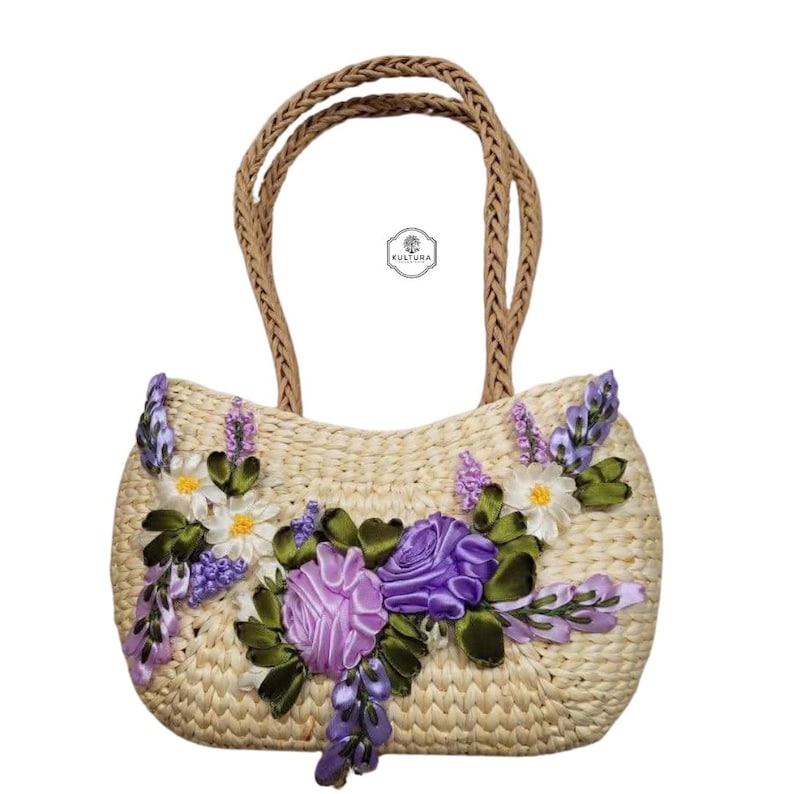 Pu&ograve; includere: Borsa a mano in paglia intrecciata con manici intrecciati, ornata da fiori di nastro lavanda, bianchi e viola. La borsa presenta una forma arrotondata e un design floreale decorativo, perfetta per trasportare l'essenziale.