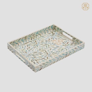 Puede incluir: Bandeja rectangular para servir con un patrón floral de hojas en tonos azules, verdes y marrones. La bandeja tiene un fondo blanco y asas integradas. La bandeja decorativa es adecuada para servir alimentos o exhibir artículos.