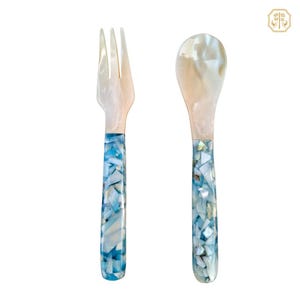 May include: A fork and spoon set. The utensils have pearlescent tops and handles with a mosaic of blue and white pieces. The fork has three tines. The spoon has a rounded bowl. The set is on a white background.